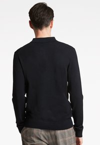 Musta pitkähihaisen poolopaita, jossa on ribattu kaulus ja hihansuut, sileä rakenne, tiukka muotoilu, yhdistettynä kuviollisiin housuihin.