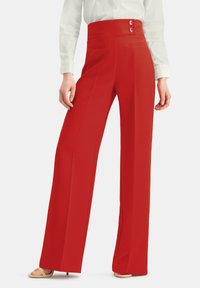 Rote hochtaillierte weit geschnittene Hose mit zwei vorderen Knöpfen, glatter Textur und seitlichen Taschen, kombiniert mit einer weißen Bluse und beigen Sandalen.