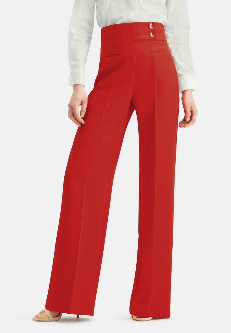 Rote hochtaillierte weit geschnittene Hose mit zwei vorderen Knöpfen, glatter Textur und seitlichen Taschen, kombiniert mit einer weißen Bluse und beigen Sandalen.