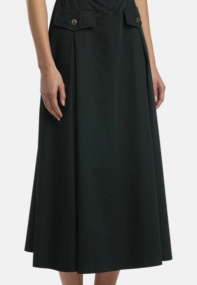 Schwarzer Midirock mit Falten und mit Knöpfen versehene Klappentaschen, getragen von einer Person mit entspannt an den Seiten hängenden Händen.