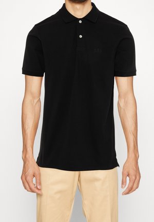 Zwarte polo met een zachte textuur, twee knopen aan de voorkant en een discreet GAP-logo op de borst. Gecombineerd met lichtbeige broek.
