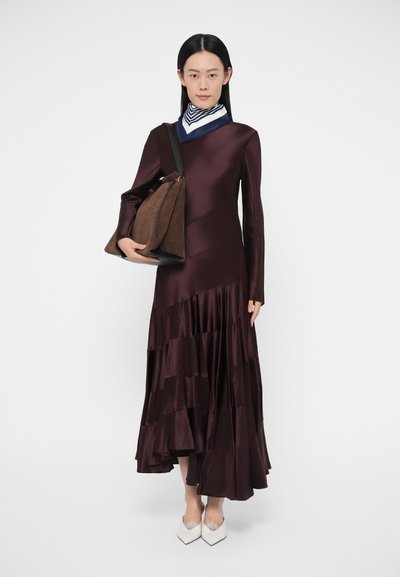 Garš bordo krāsas satīna kleita ar kārtotām volānu detaļām, garām piedurknēm un diagonālu šuvi. Kombinēta ar brūnu zamšādas somu un baltām smailām kurpēm.