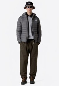 Chaqueta acolchada gris con patrón acolchado horizontal, combinada con una sudadera gris, pantalones cargo oliva y botas negras; los accesorios incluyen un sombrero tipo bucket negro y gafas de sol.