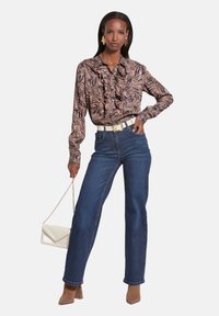 Langarmshirt met ruffle-detail, tan en donkerbruin bladerenprint; hoge taille blauwe jeans; beige vierkante hakken; witte handtas.