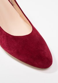 Gros plan sur l'avant d'une chaussure plate en daim rouge pour femme avec un bout arrondi et une doublure intérieure beige sur fond blanc.