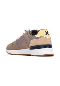 Zapatillas para hombre con gamuza marrón claro, paneles de textil gris, un acento amarillo en el talón y una suela blanca con una banda de rodadura de goma marrón.