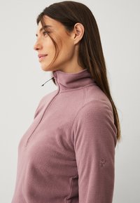 Rosa fleece pullover med en halv-zip krave. Har flatlock sømme og et lille, broderet logo på venstre ærme.