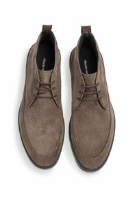 Braune Wildleder-Chukka-Stiefel mit flachen Schnürsenkeln und runder Zehenpartie. Sie verfügen über eine flache schwarze Gummisohle und genähte Akzente für zusätzliche Details.