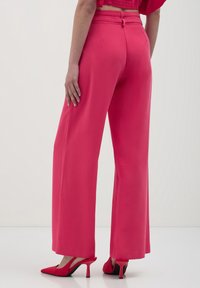 Pantalons larges roses vif en tissu lisse, dotés d'une taille ajustée et d'une fermeture éclair au dos. Associés à des talons assortis.