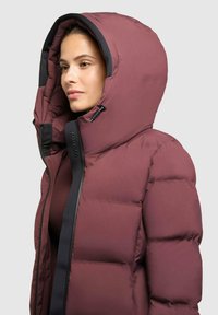 Bordeauxfarbener Pufferjacke mit einer großen Kapuze, ausgestattet mit einem schwarzen Reißverschluss und Akzenten. Der Stoff sieht glatt und isoliert aus und hat eine gesteppte Textur.