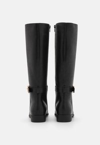 Botas de imitación de cuero negro hasta la rodilla con un acabado suave, que cuentan con un cierre lateral y una correa decorativa con hebilla en el tobillo.