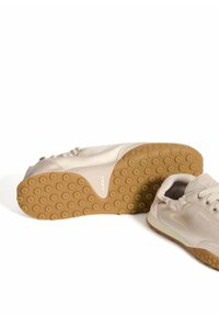 Zapatillas deportivas beige con parte superior sintética lisa y suelas de goma texturizada que presentan agarres circulares. El logo "HOFF" es visible.