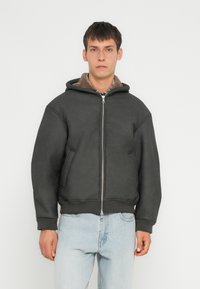 Veste à capuche gris foncé avec une fermeture éclair à l'avant, poches latérales et doublure intérieure en peluche. Manches et ourlet élastiques, avec une coupe décontractée.