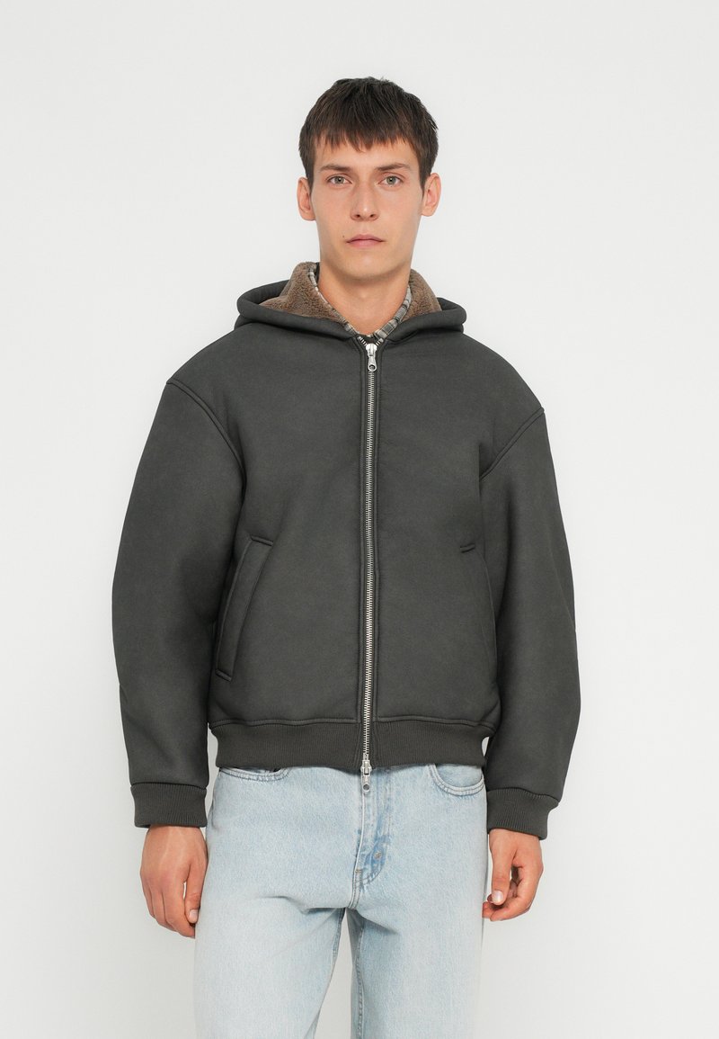 Veste à capuche gris foncé avec une fermeture éclair à l'avant, poches latérales et doublure intérieure en peluche. Manches et ourlet élastiques, avec une coupe décontractée.