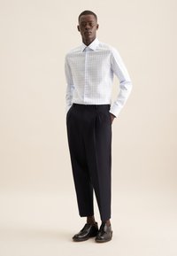 Camicia a quadri blu chiaro e bianca con colletto, abbinata a pantaloni neri a vita alta e scarpe nere con finitura liscia.