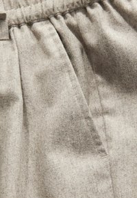 Světle šedá tkanina s texturovaným povrchem, která má na bocích stažený elastický pas a boční kapsy, ukazuje jemné variace v barvě.