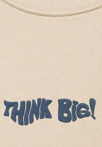 Tessuto a maglia beige con scollo a costine, con un audace testo blu che recita "PENSATE IN GRANDE!" in un font giocoso e arrotondato.