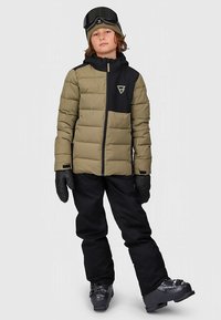 Minkšta alyvuogių žalios spalvos striukė su juodais akcentais, juodos slidinėjimo kelnės, pirštinės ir slidinėjimo batai. Modelis vilki megztą kepurę ir akinius nuo slidinėjimo.