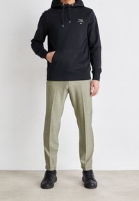 Felpa nera con cappuccio e tasca frontale, con dettagli del logo bianchi. Abbinate a pantaloni sartoriali verde oliva chiaro e sneakers nere.
