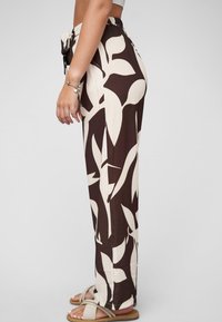 Pantalons à motifs marron et crème, avec une coupe décontractée, une taille élastique et des poches latérales. Fabriqués en tissu léger avec une texture douce.