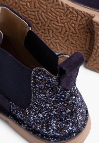 Pantofi slip-on navy cu un panou lateral strălucitor și texturat, inserții elastice și o talpă din cauciuc maro cu un model de prindere.