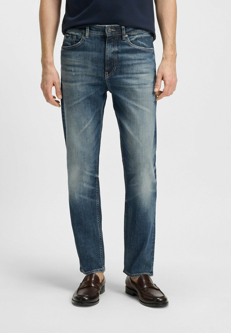 Jeans in denim blu con una finitura sbiadita, taglio dritto, design a cinque tasche e cuciture a vista. Abbinati a mocassini marroni.