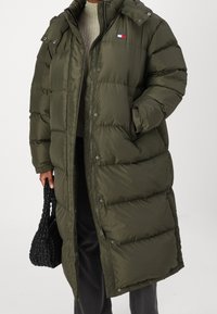 Olivgrön puffjacka med lång design, med dragkedja fram, tryckknappar och en liten logotypdetalj på bröstet. Texturerat tyg.