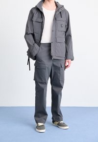 Gray jacket with multiple front pockets, zip closure, and a hood, paired with gray cargo pants featuring side pockets and elastic waistband.