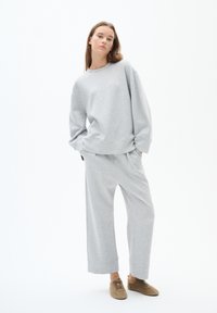 Grijze sweatshirt en bijpassende wijde broek, met een ontspannen pasvorm, zachte textuur en ribgebreide randen. Gepaarde met fuzzy bruine slippers.