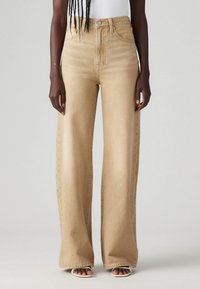 Jeans a gamba larga in denim beige chiaro con vita alta, caratterizzati da un classico design a cinque tasche e da una leggera sfumatura per aggiungere texture.