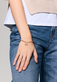 Złota bransoletka łańcuszkowa z charmsami w kształcie serca i gwiazdy, noszona na ręce. Ręka jest ułożona na niebieskim denimu.