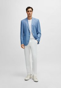 Ljusblå kavaj med två knappar, spetsiga slag, i kombination med en vit t-shirt och vita byxor. Skorna är vita med beige detaljer.