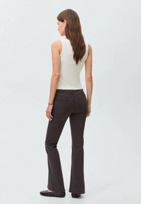 Top de tirantes crema combinado con vaqueros acampanados de un gris oscuro. Los vaqueros tienen una textura suave y una costura sutil, con bolsillos en la parte trasera.