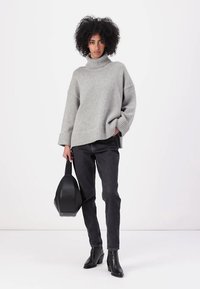 Suéter gris de gran tamaño con cuello alto y dobladillos acanalados, combinado con jeans negros de pierna recta y botas de tacón negro hasta el tobillo, sosteniendo un bolso negro.