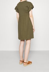 Oliwkowa sukienka z krótkimi bufkami, zebranym w pasie, o luźnym kroju. Zestawiona z brązowymi zamszowymi espadrylami.