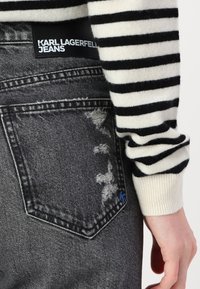 Black and white striped sweater paired with distressed gray jeans featuring a rectangular pocket and blue logo accent.