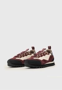 Sneakers w kolorze burgundu i kremowym, z tekstylną cholewką, czarną gumową podeszwą, złotymi oczkami i wyściełanym kołnierzem. Charakterystyczny, wytrzymały wzór bieżnika.