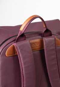 Zaino bordeaux con manico superiore in pelle beige, spallacci imbottiti e tessuto liscio con dettagli di cucitura.