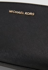 Czarny portfel o teksturowanej powierzchni z złotym logo "MICHAEL KORS". Posiada gładką linię i subtelne wzory, sugerujące materiał syntetyczny.