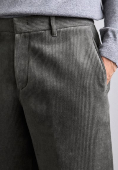 Pantaloni in corduroy grigio con righe verticali, dotati di tasche laterali e vita strutturata, parzialmente visibili su uno sfondo chiaro.