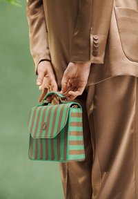 Striped handbag featuring green and brown tones, textured surface, flap closure, and a top handle, held by a person in a brown outfit.