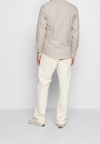 Lichtbeige langemouwen overhemd van linnen, gecombineerd met crèmewitte broek. Het overhemd heeft een kraag met knopen en manchetten.