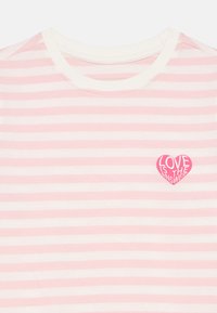 Ροζ και λευκή ριγέ μπλούζα με μπαλώμα σε σχήμα καρδιάς που γράφει "Η ΑΓΑΠΗ ΕΙΝΑΙ Η ΑΠΑΝΤΗΣΗ." Μαλακό ύφασμα και στρογγυλή λαιμόκοψη.