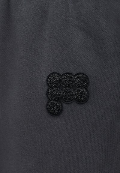 Μαύρο ύφασμα με υφασμένο μαύρο έμβλημα που αποτελείται από επτά στρογγυλούς, ανυψωμένους βρόχους διατεταγμένους σε τετράγωνο με έναν βρόχο από κάτω.