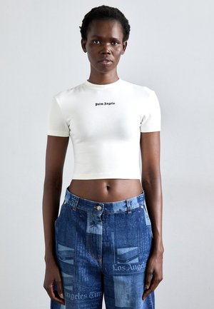 Cropped white short-sleeve shirt with 'Palm Angels' text; paired with blue denim jeans featuring newspaper print and a relaxed fit.