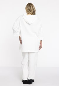 Witte relaxte loungewear set bestaande uit een hoodie met capuchon en rechte broeken, gemaakt van een textuurstof met een subtiel ruitpatroon.