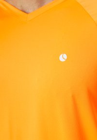 Orange v-neck t-shirt made of textured fabric featuring a small white logo on the left chest area. Smooth surface, medium thickness.
