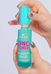 Teal plastflaska med en turkos pumpkåpa märkt "ZINC POWER." Har en matt yta och rosa text som beskriver produktanvändning.
