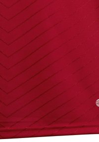 Tessuto rosso con un motivo a zigzag in rilievo di un rosso leggermente più scuro. Texture liscia con una sottile lucentezza e un piccolo logo a forma di globo in un angolo.