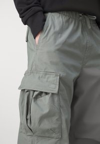 Cargo-byxor i en ljus olivfärg gjorda av lätt tyg, med dragsko i midjan och sidofickor med lock.